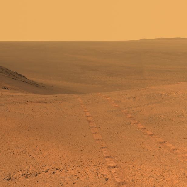 Eine weite, orangefarbene Landschaft mit Reifenspuren auf der Oberfläche.