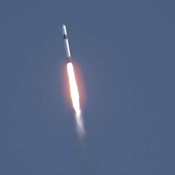 Eine Rakete startet mit einer hellen Flamme in den Himmel; NASA-Logo sichtbar.