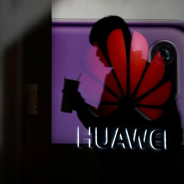 A man walking past a Huawei P20 smartphone advertisement is reflected in a glass door in front of a Huawei logo, at a shopping mall in Shangha