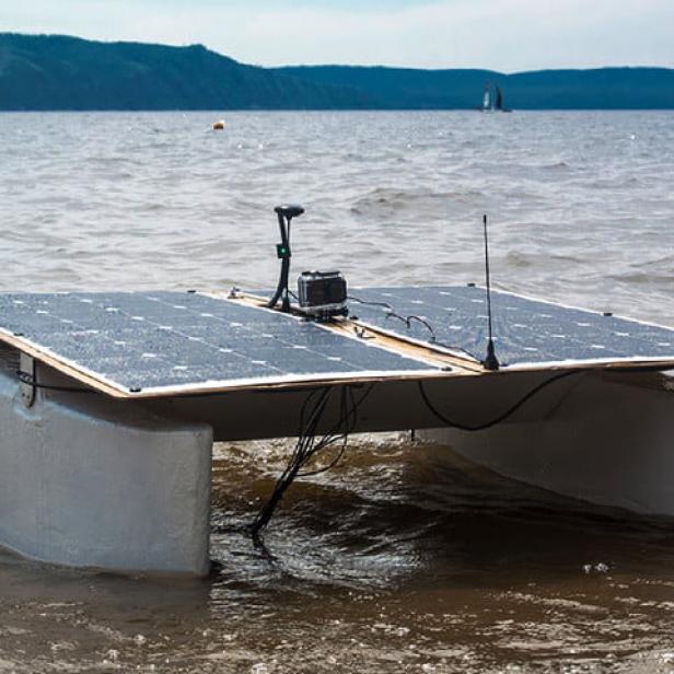 Ein solarbetriebenes Katamaran-Boot liegt im flachen Wasser am Ufer.