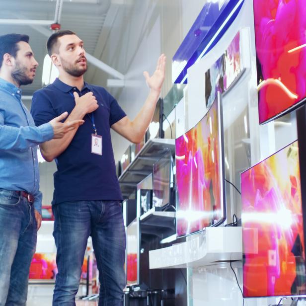 Ein Verkäufer erklärt einem Kunden die Funktionen von Fernsehgeräten in einem Geschäft.