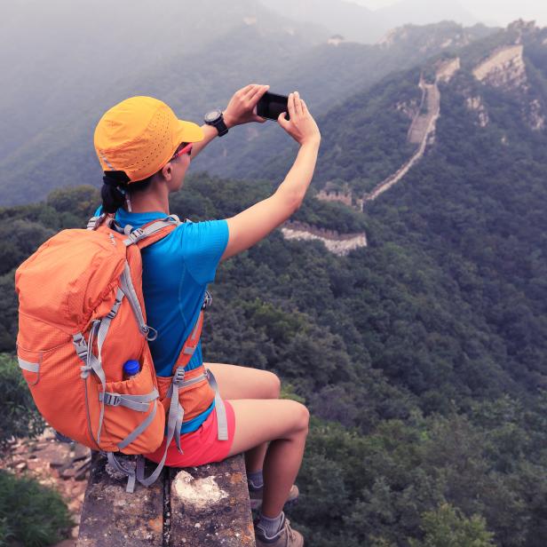 young woman hiker taking photo with smart phone on top of great wall