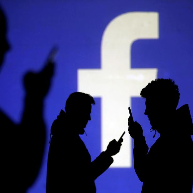 FILE PHOTO: Silhouettes of mobile users are seen next to a screen projection of Facebook logo in this picture illustration