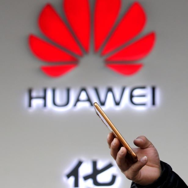 FILE PHOTO: Man holding his phone walks past a Huawei shop in Beijing