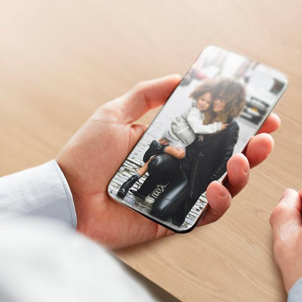 Eine Person hält ein Smartphone mit dem Foto einer Mutter, die ihr Kind Huckepack trägt.