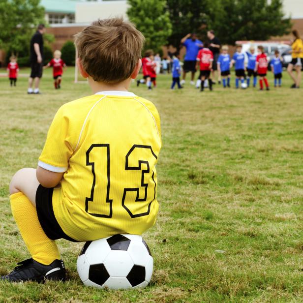 Young boy child in uniform watching organized youth soccer or football game from sidelines