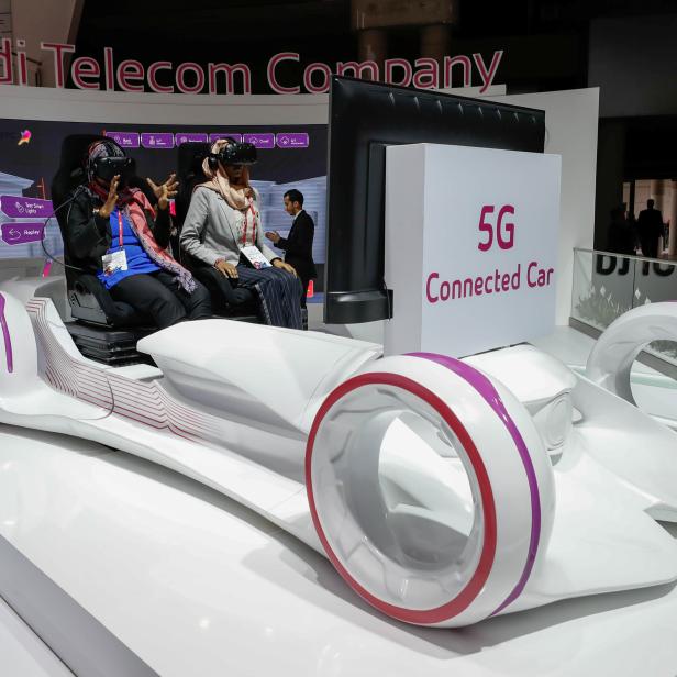 Women sit in a 5G connected car simulator displayed at the Saudi Telecom Company stand during the Mobile World Congress in Barcelona