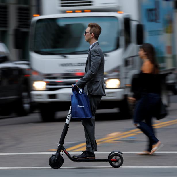 A man in a suit rides an electric BIRD rental scooter along a city street in San Diego, California