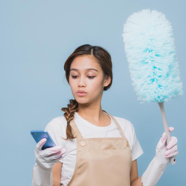 Young woman watching smart phone while house cleaning while cleaning.