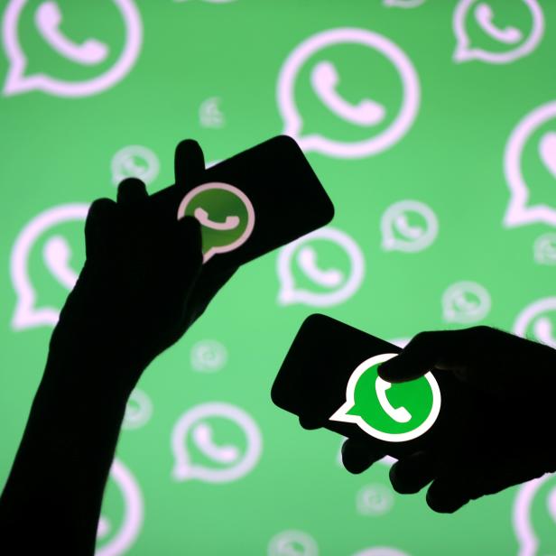 FILE PHOTO: Men pose with smartphones in front of displayed Whatsapp logo in this illustration