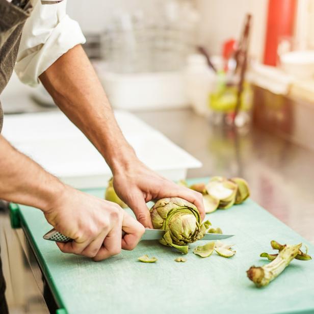 Chef cutting artichokes for dinner preparation - Man cooking inside restaurant kitchen - Focus on vegetable - Vegan cuisine, lifestyle and healthy food concept