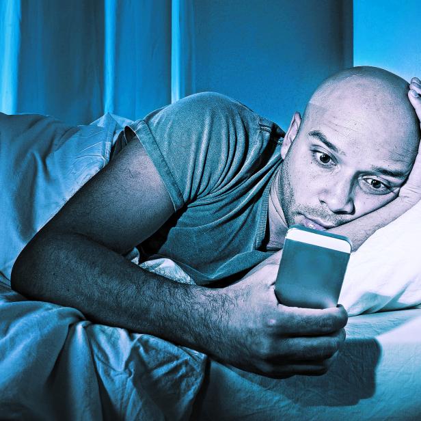young cell phone addict man in bed using smartphone