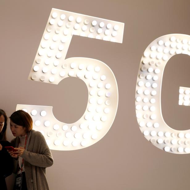 Visitors use their mobiles phones as they stand next to a 5G Led Smart Bulb panel inside the Xiaomi booth at the Mobile World Congress in Barcelona