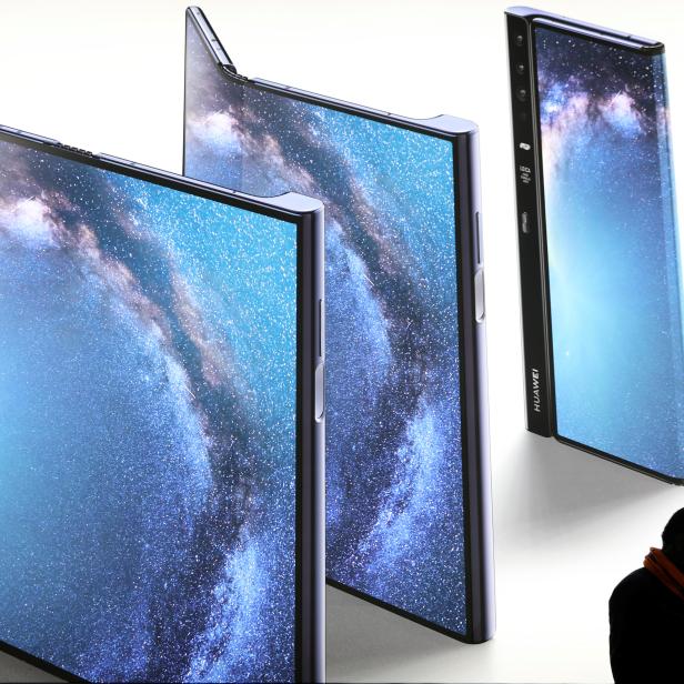 A man checks his phone next to an advertisement of a new Huawei Mate X device at the Mobile World Congress in Barcelona