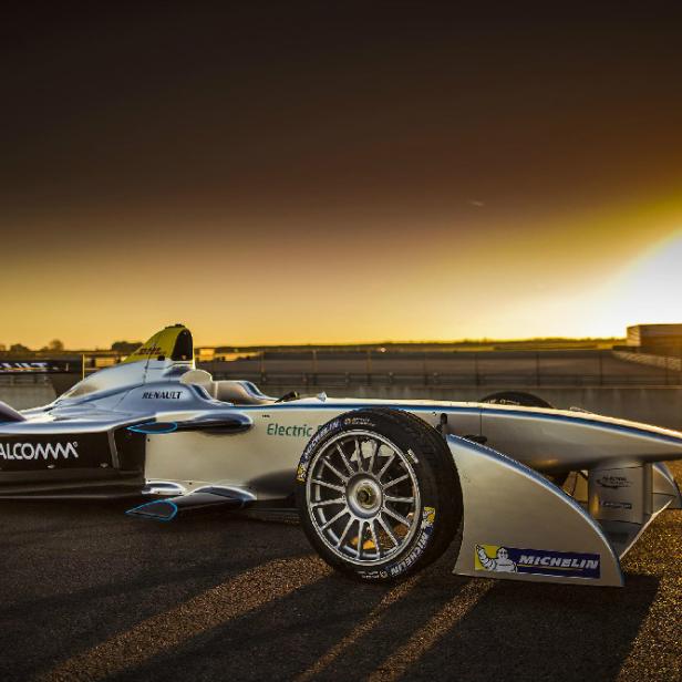 Ein silbernes Formel-E-Rennauto steht auf einer Rennstrecke im goldenen Abendlicht.
