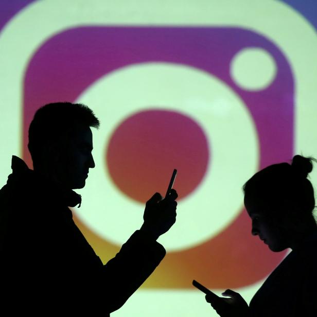 FILE PHOTO: Silhouettes of mobile users are seen next to a screen projection of Instagram logo in this picture illustration