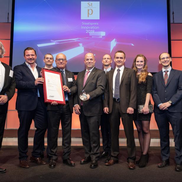 Eine Gruppe von Personen posiert mit einer Urkunde und einem Preis für den „Staatspreis Innovation 2019“.