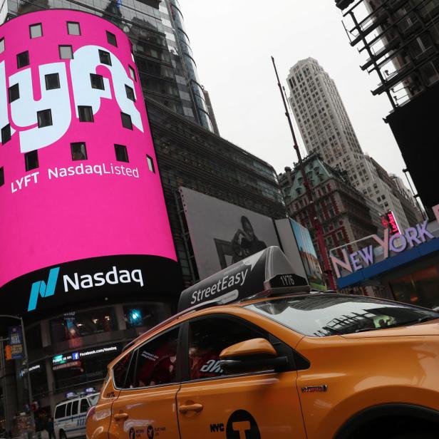Ein gelbes Taxi vor den leuchtenden Werbetafeln von Lyft und Nasdaq am Times Square in New York.