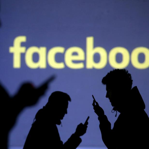 FILE PHOTO: Silhouettes of mobile users are seen next to a screen projection of Facebook logo in this picture illustration