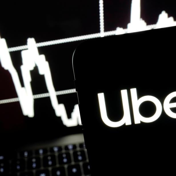 Logo of the Uber is seen on a smartphone screen as a picture of stock exchange graph is displayed on a computer screen in this illustration picture