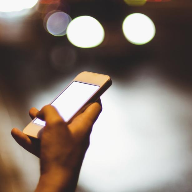 Eine Hand hält ein Smartphone mit hellem Bildschirm im Dunkeln.