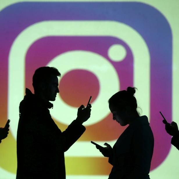 FILE PHOTO: Silhouettes of mobile users are seen next to a screen projection of Instagram logo in this picture illustration