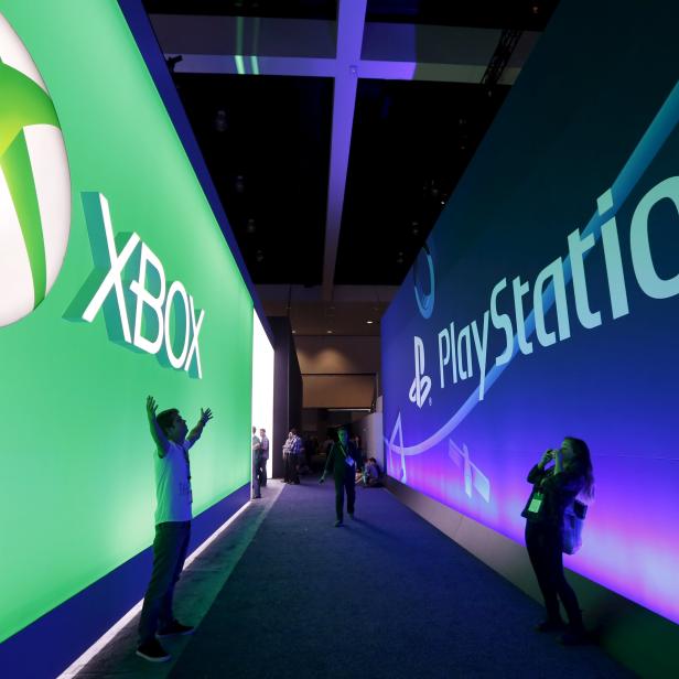 A man poses for a photo in front of a Microsoft Xbox sign opposite a Sony PlayStation sign at the Electronic Entertainment Expo, or E3, in Los Angeles