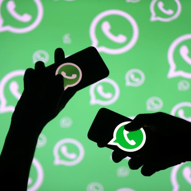 FILE PHOTO: Men pose with smartphones in front of displayed Whatsapp logo in this illustration