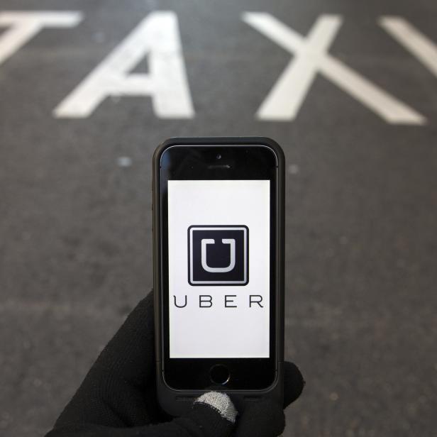 Photo illustration of logo of car-sharing service app Uber on a smartphone over a reserved lane for taxis in a street in Madrid