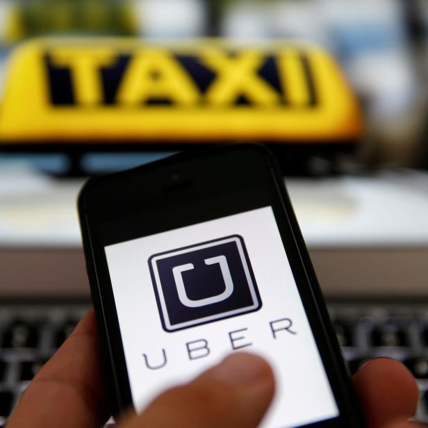 FILE PHOTO: An illustration picture shows the logo of car-sharing service app Uber on a smartphone next to the picture of an official German taxi sign