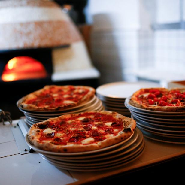 Mehrere Pizzen stehen auf Tellern vor einem Pizzaofen.