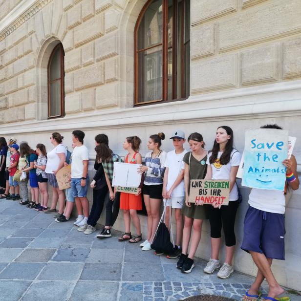 Eine Gruppe junger Menschen demonstriert mit Schildern vor einem Gebäude.