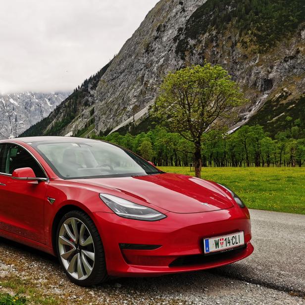 Ein rotes Tesla-Auto vor einer Berglandschaft.
