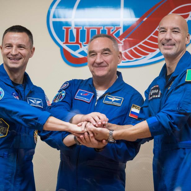 Drei Astronauten in blauen Raumanzügen legen ihre Hände übereinander.