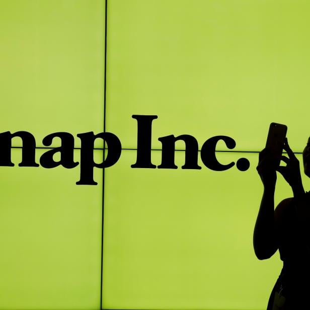 FILE PHOTO: A woman stands in front of the logo of Snap Inc. on the floor of the New York Stock Exchange (NYSE) while waiting for Snap Inc. to post their IPO, in New York City