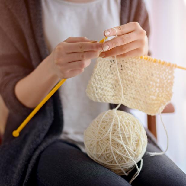 Eine Frau strickt mit gelben Nadeln an einem hellen Wollstück.