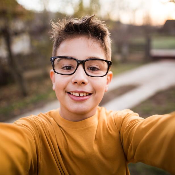 Ein lächelnder Junge mit Brille macht ein Selfie im Freien.