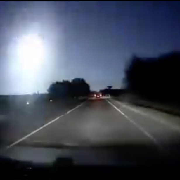 Ein heller Meteor ist am Nachthimmel über einer Straße zu sehen.