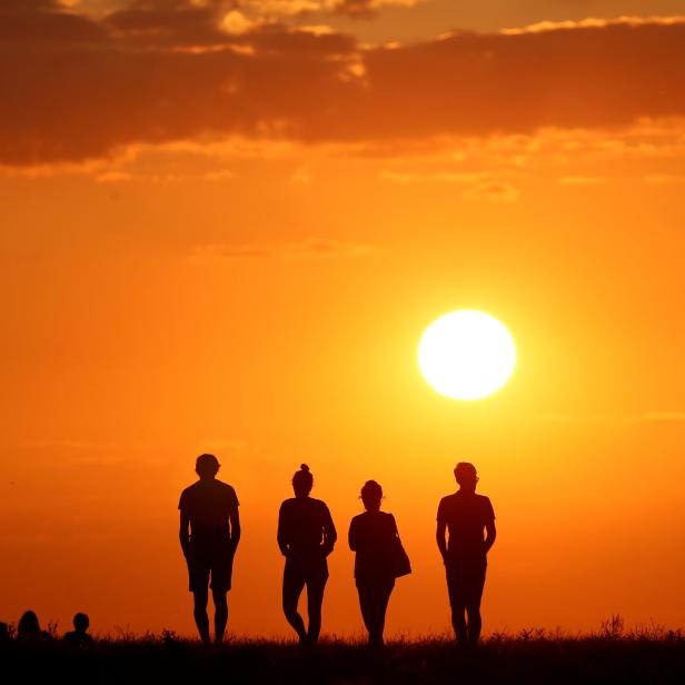 People are silhouetted against the setting sun on top of the Drachenberg in Berlin