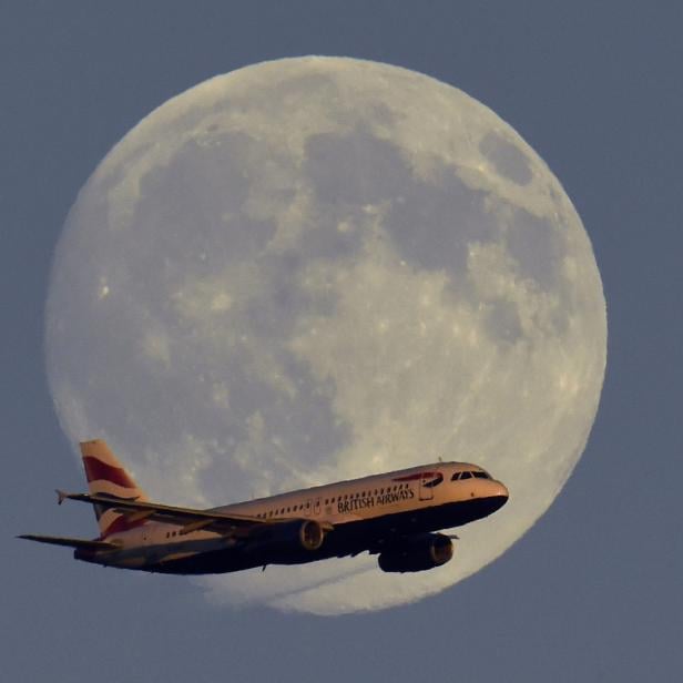 A British Airways passenger aircraft passes in front of the moon as it makes it's landing approach towards Heathrow Airport in west London in this photograph taken on July 18, 2016.