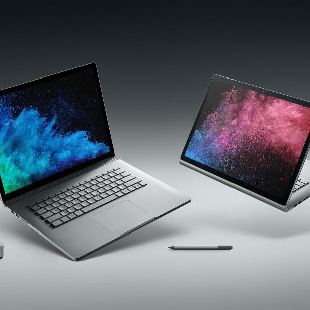 Zwei geöffnete Laptops mit farbenfrohen Bildschirmen, ein Stift und ein Ziffernblatt liegen auf einem Tisch.