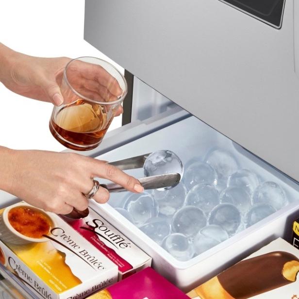 Eine Person nimmt mit einer Zange einen Eisball aus dem Eiswürfelbehälter eines Kühlschranks.