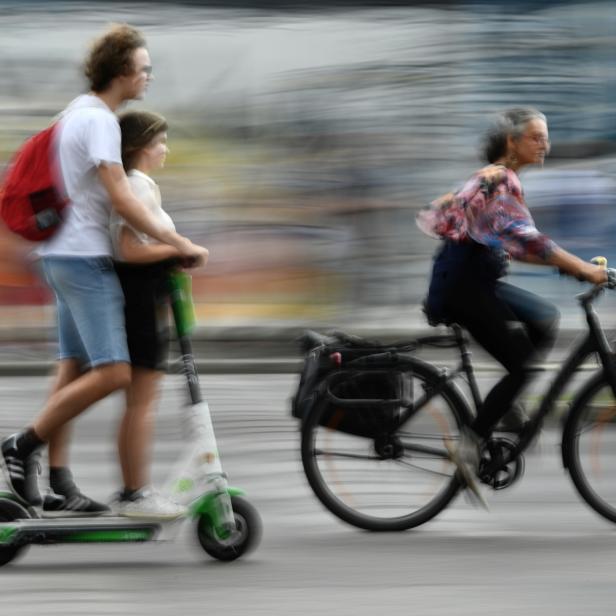 A cyclist passes two people riding an E-Scooter in Berlin