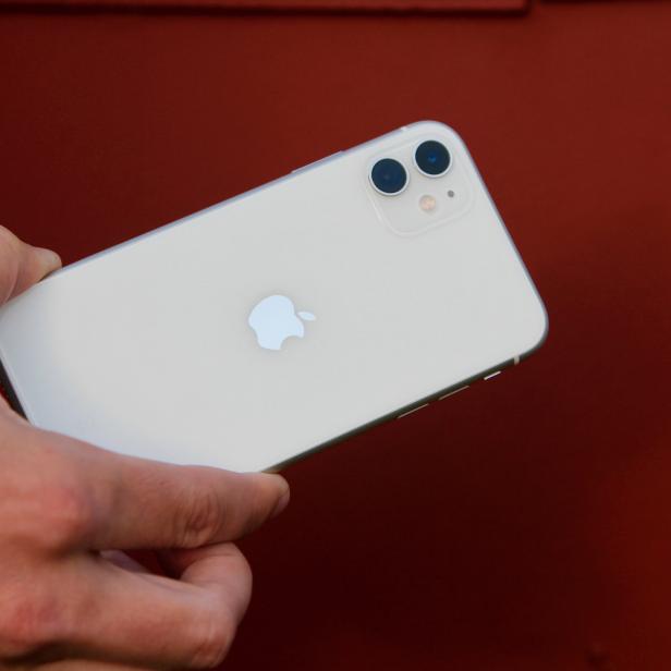 Eine Hand hält ein weißes iPhone vor einem roten Hintergrund.