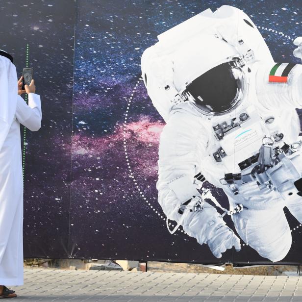 Ein Mann im traditionellen Gewand fotografiert ein Bild eines Astronauten mit der Flagge der Vereinigten Arabischen Emirate.