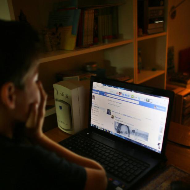 Ein Junge sitzt vor einem Laptop und schaut auf Facebook.