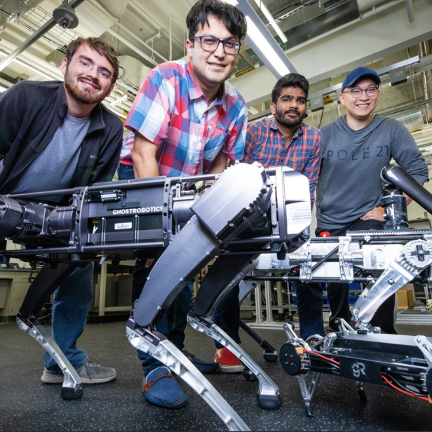 Vier Personen posieren mit zwei vierbeinigen Robotern von Ghost Robotics in einem Labor.