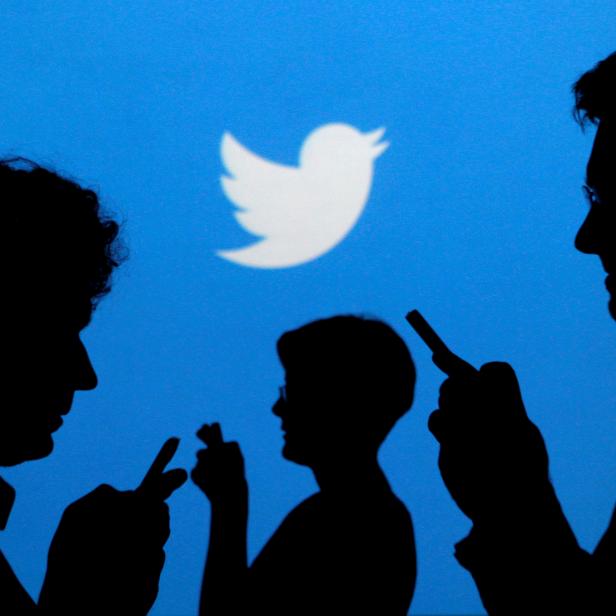 FILE PHOTO: People holding mobile phones are silhouetted against a backdrop projected with the Twitter logo