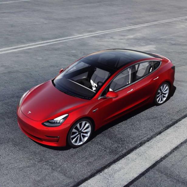 Ein rotes Tesla Model 3 auf einer asphaltierten Straße.
