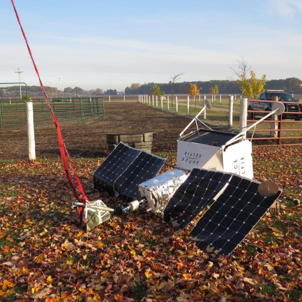 Ein zerlegtes Satellitenmodell liegt auf einem Feld voller Herbstlaub.